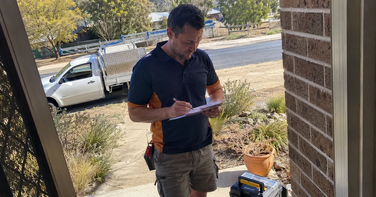 Handyman writing a quote on a clipboard at the front door of a Canberra home