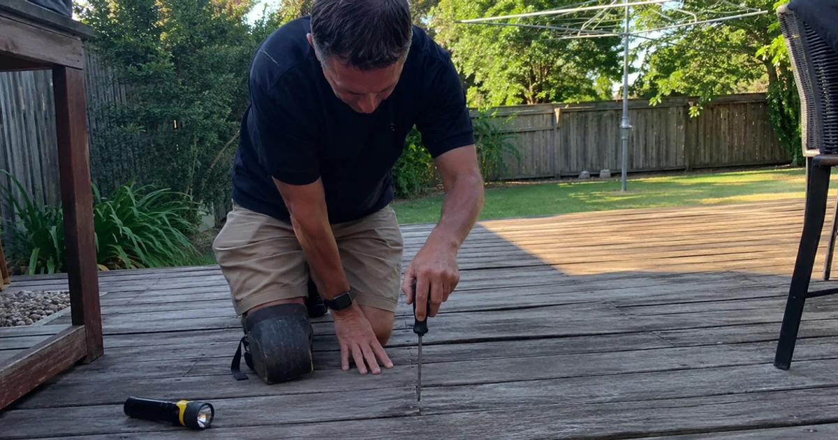Handyman probing a soft rotting deck board with a screwdriver