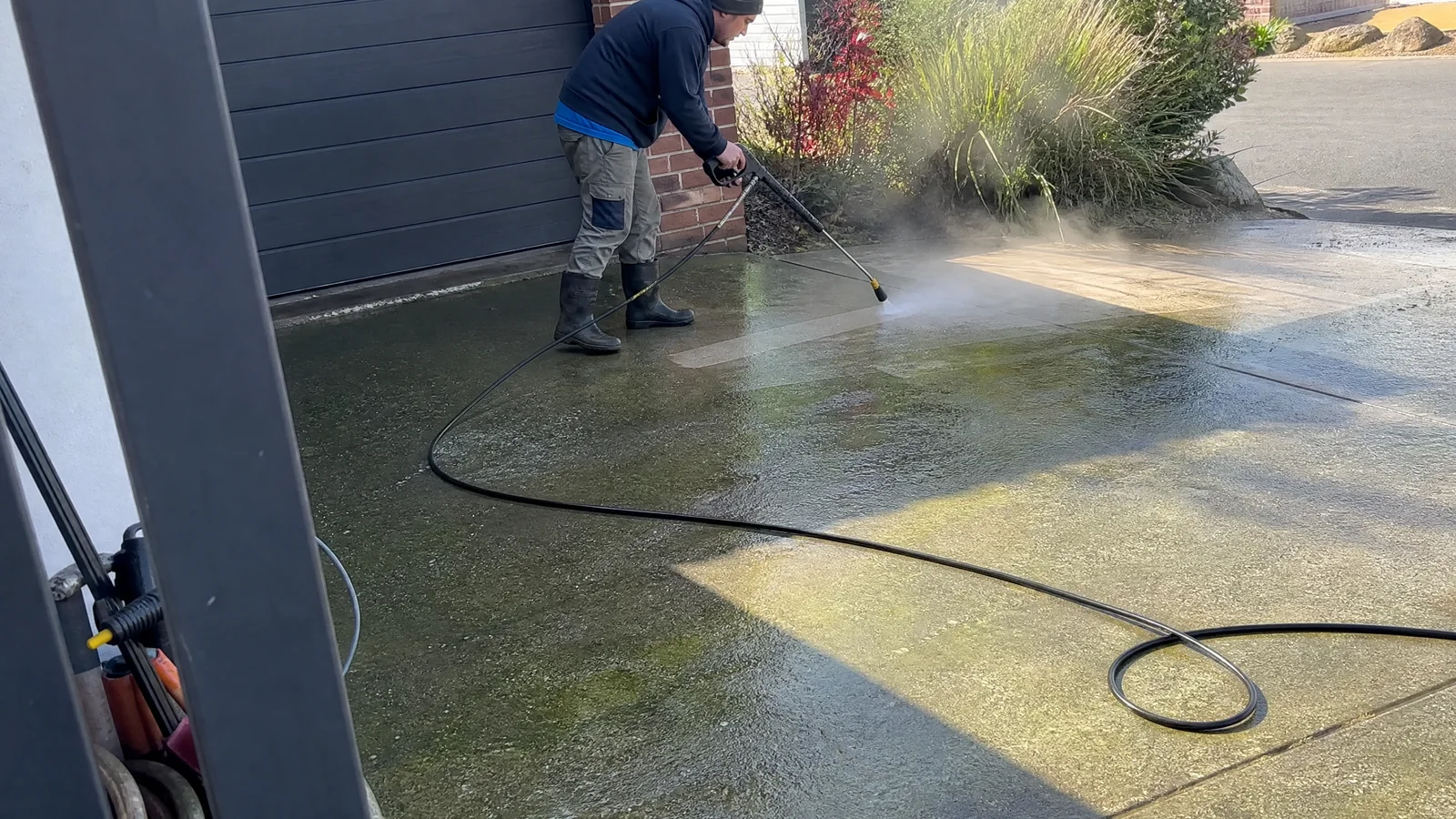 Tradesman pressure washing a green-stained concrete driveway in Canberra